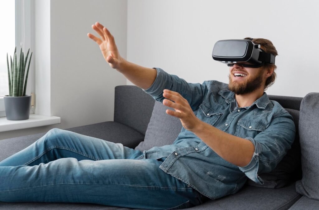 Homem sorridente deitado em um sofá usando um óculos de realidade virtual, que é um exemplo de wearable tech.
