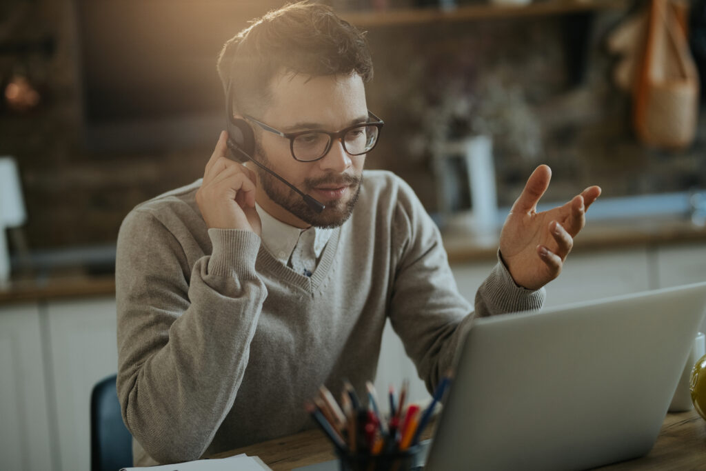 Homem jovem em um ambiente corporativo com fone de ouvido atendendo a um chamado de ITSM ou ISM no computador.