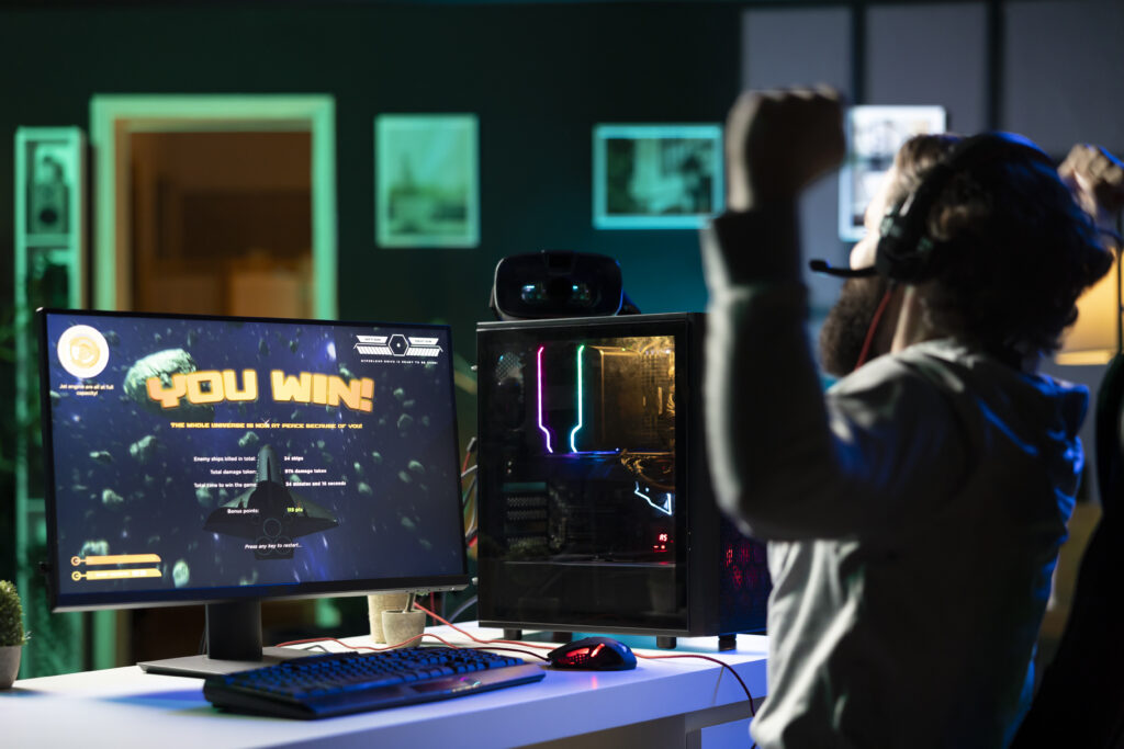 Homem usando fones de ouvido celebrando após vencer um jogo de gamificação no computador.