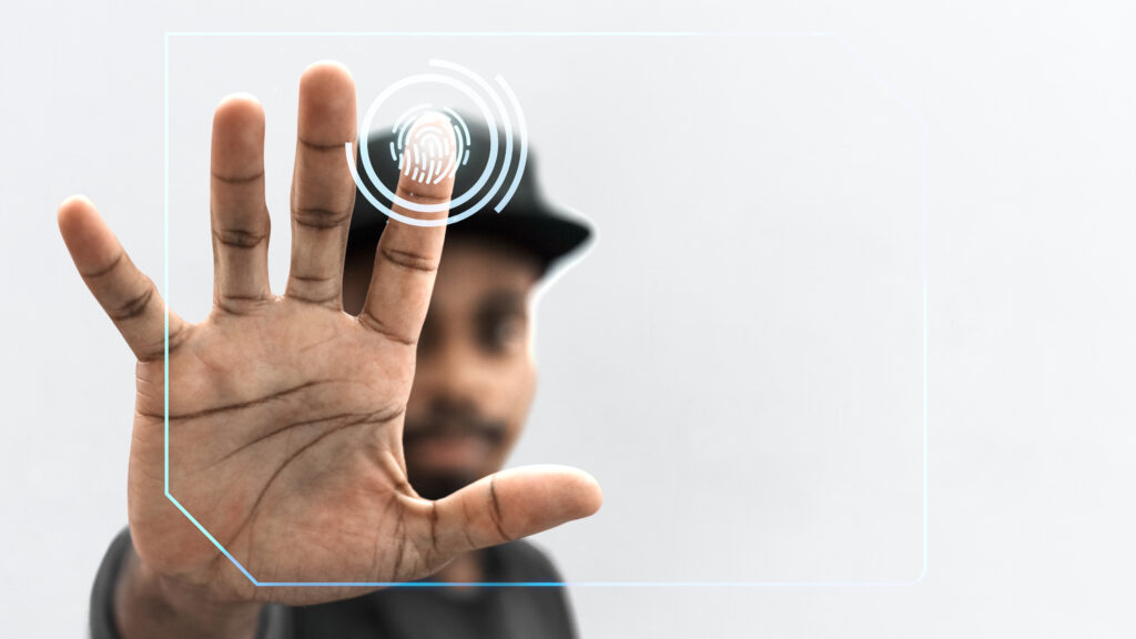 Autenticação sem senha para empresas: saiba a diferença entre senhas e passwordless 1 Homem com a mão direita aberta tocando com o dedo indicador uma impressão digital em holografia, representando a biometria, um tipo de autenticação sem senha para empresas.
