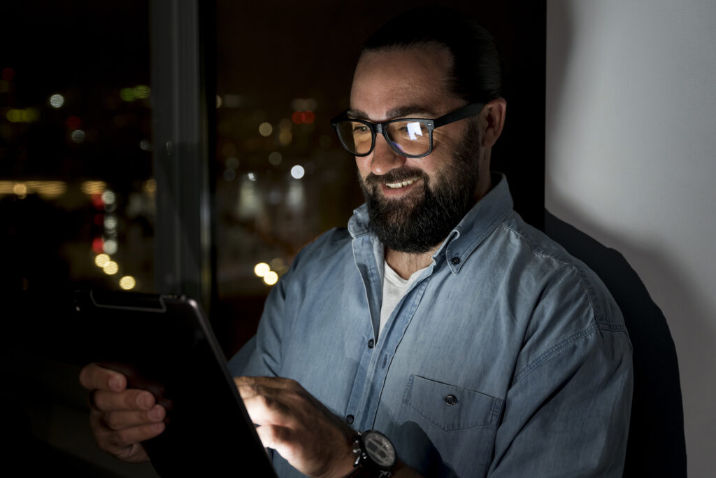 Shadow AI: o que é e como transformá-lo em vantagem competitiva 1 Homem de óculos em uma sala, utilizando um tablet com ferramentas de IA, representando o shadow AI.