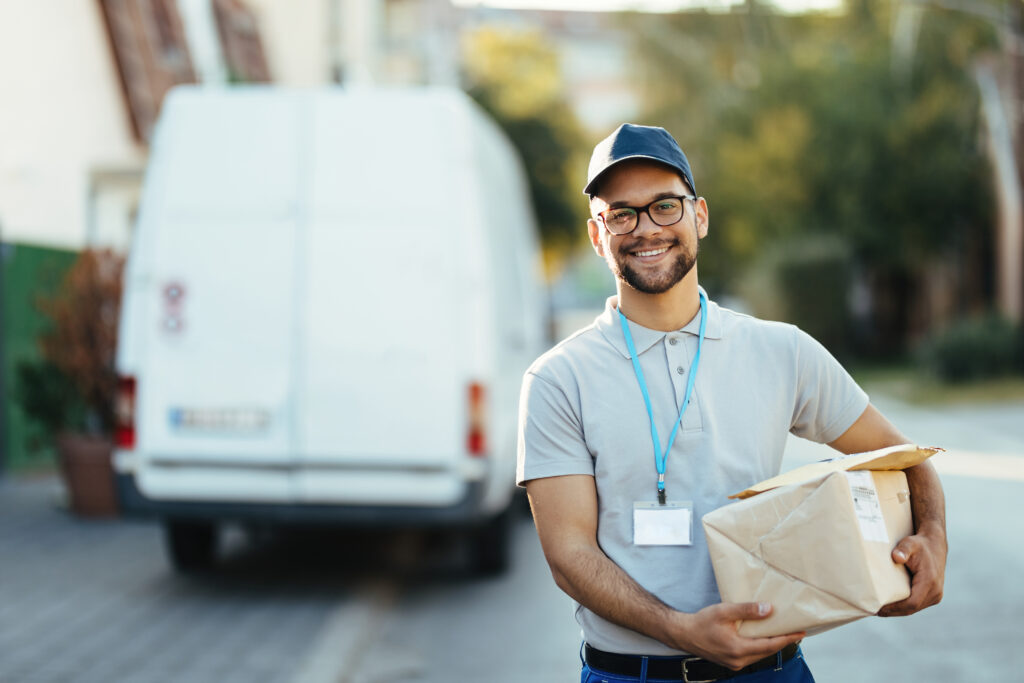 Um homem sorridente segura um pacote de entrega, em frente a uma van.