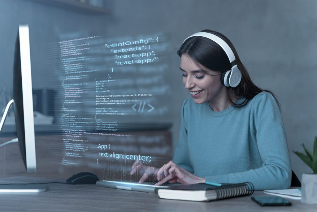 Uma mulher usando fones de ouvido, sentada em uma estação de trabalho enquanto desenvolve um software sob medida para empresas.