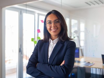 Confident Latin business leader portrait. Young businesswoman in suit and glasses posing with arms folded, looking at camera and smiling. Female leadership concept