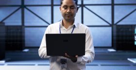 Engineer in server farm checking recovery plan on laptop, monitoring data center energy consumption across components, making sure sensors are functioning optimally, doing maintenance on equipment