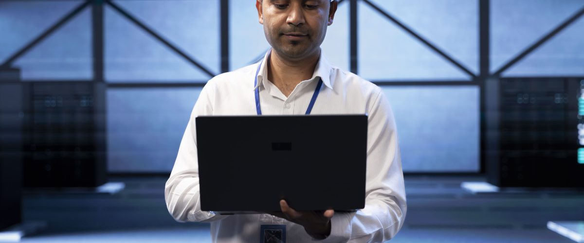 Engineer in server farm checking recovery plan on laptop, monitoring data center Engineer in server farm checking recovery plan on laptop, monitoring data center energy consumption across components, making sure sensors are functioning optimally, doing maintenance on equipment