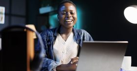 Black woman enjoying a comedy movie on her digital laptop, while seated at desk in her apartment. Excited african american lady using personal computer for virtual online communication with friends.