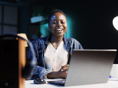 Black woman enjoying a comedy movie on her digital laptop, while seated at desk in her apartment. Excited african american lady using personal computer for virtual online communication with friends.
