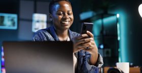 Female student using mobile device Cheerful female college student using mobile device to engage with friends on social media platforms. African american lady using cell phone to surf the web while sitting at desk in her home office.