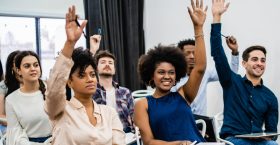 Group of young people sitting on conference together while raising their hands to ask a question. Business team meeting seminar training concept.