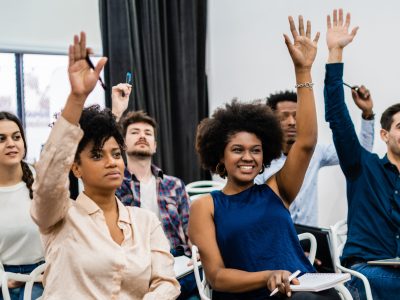 Group of young people sitting on conference together while raising their hands to ask a question. Business team meeting seminar training concept.