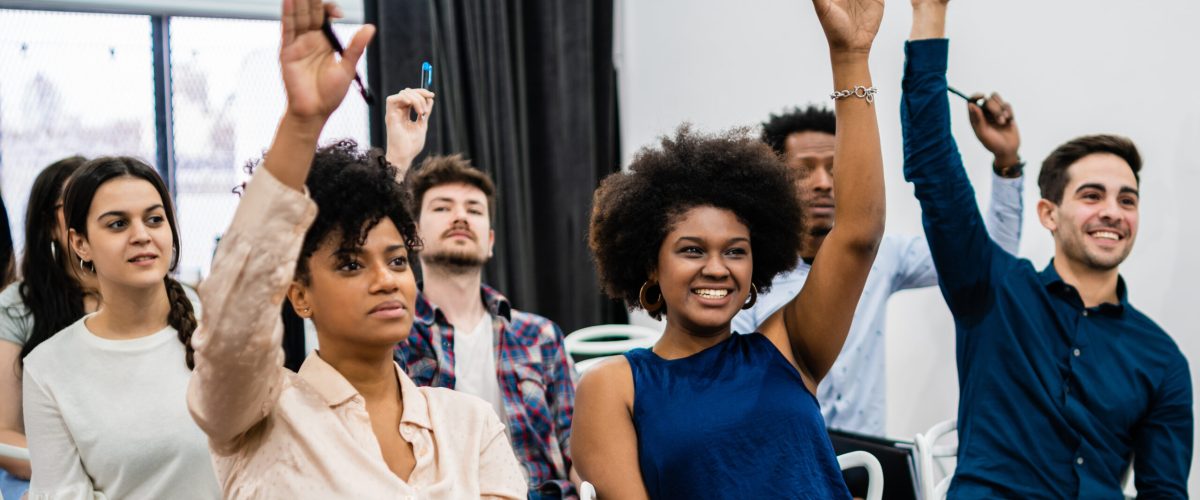 Group of young people sitting on conference together while raising their hands to ask a question. Business team meeting seminar training concept.