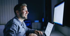 Happy employee working on the project and sitting in the office late at night. Hands on keyboard.