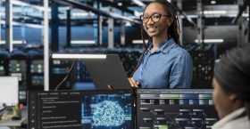 Happy specialist inspecting neural network data center used for machine learning. Portrait of smiling engineer doing maintenance on server hub to optimize it for artificial intelligence workloads.