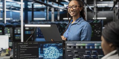 Happy specialist inspecting neural network data center used for machine learning. Portrait of smiling engineer doing maintenance on server hub to optimize it for artificial intelligence workloads.