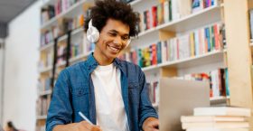 Intelligent Latin student guy sitting at desk, writing in copybook, having lecture or webinar, studying in college library. Education, new skills Intelligent Latin student guy sitting at desk, writing in copybook, having lecture or webinar, studying in college library. Education, new skills