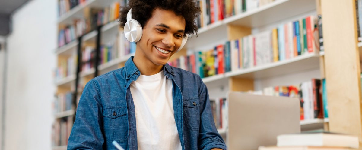 Intelligent Latin student guy sitting at desk, writing in copybook, having lecture or webinar, studying in college library. Education, new skills Intelligent Latin student guy sitting at desk, writing in copybook, having lecture or webinar, studying in college library. Education, new skills