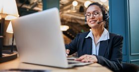 Joyful young woman demonstrating her smile while looking at screen of her laptop