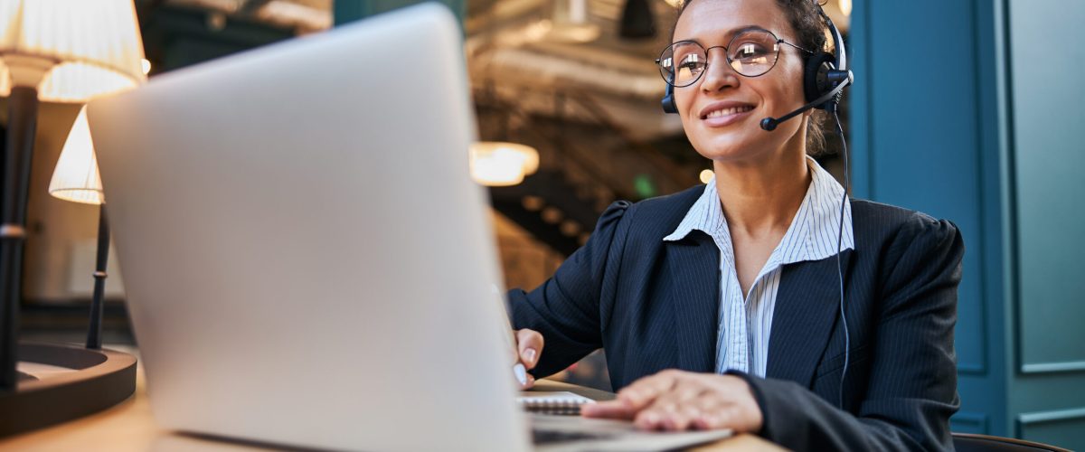 Joyful young woman demonstrating her smile while looking at screen of her laptop