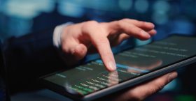 Male system administrator inspecting big data on tablet, working in modern data center. Infrastructure specialist inspecting server rack systems, artificial intelligence. Handheld shot. Close up.