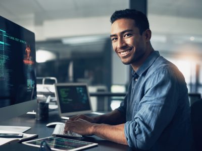 Portrait, man and smile of programmer on computer in office workplace at night. IT, face and male coder or person programming, coding and writing for software development or information technology