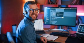 Sitting and smiling. Professional programmer is working indoors. Neon lighting Sitting and smiling. Professional programmer is working indoors. Neon lighting.