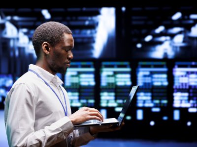 African american system administrator typing supercomputer hub contingency plan on laptop to provide fast restoration of service, limiting damage and minimizing interruptions to normal operations